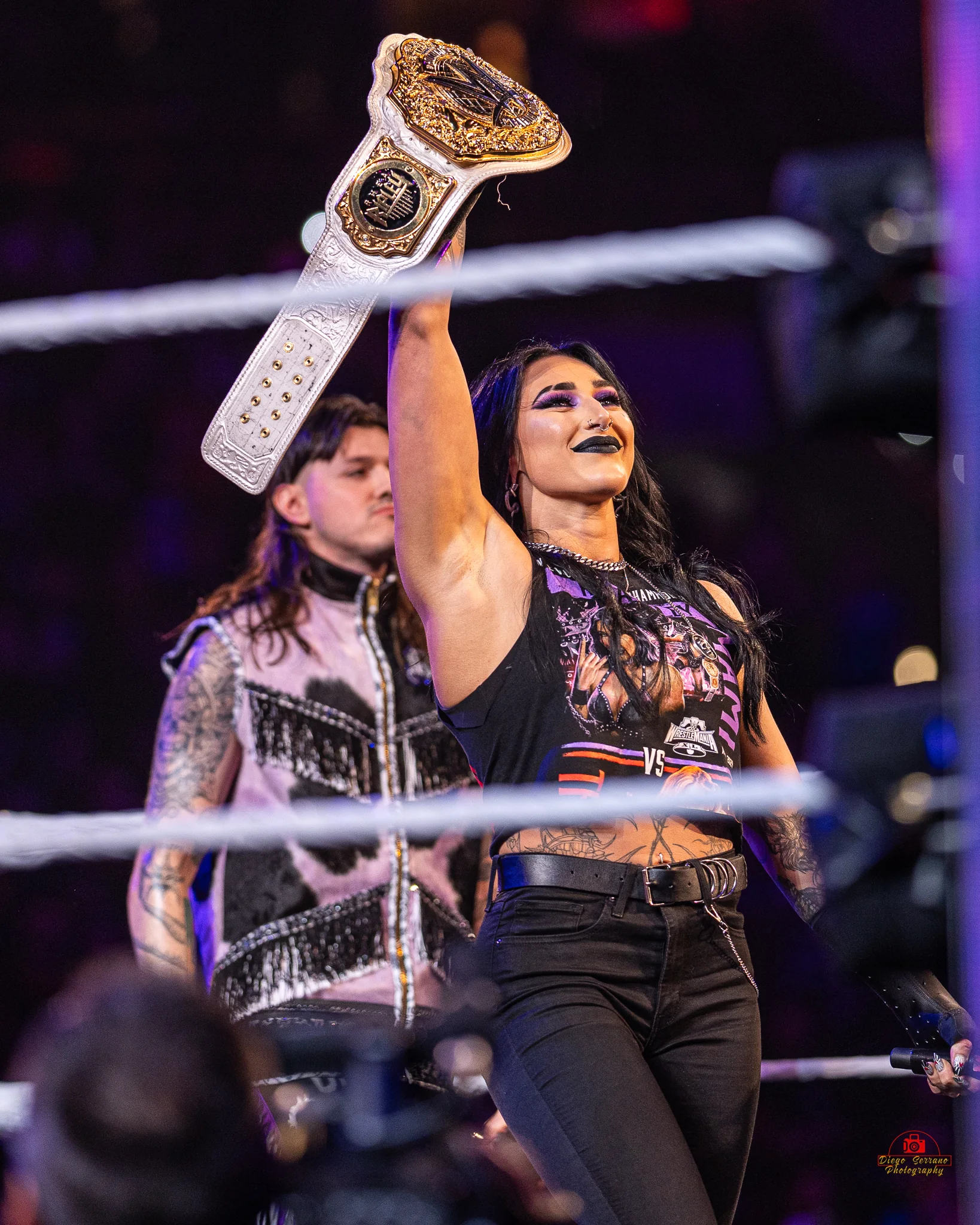 Rhea Ripley posing with a WWE championship belt featuring personalized side-plate positions