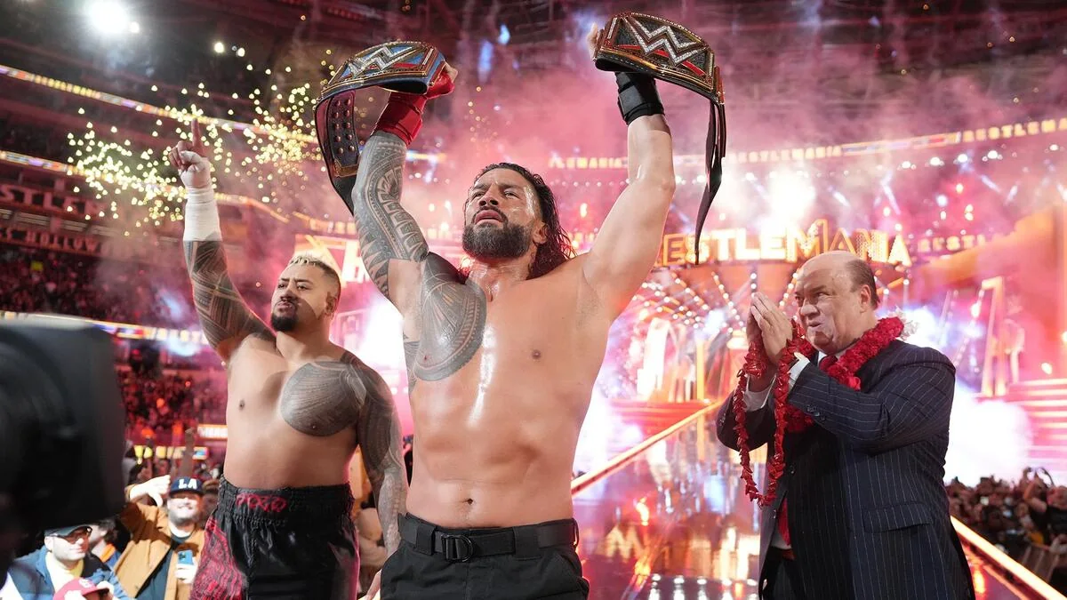 Roman Reigns wearing his signature black glove while raising two WWE championship titles at WrestleMania 39